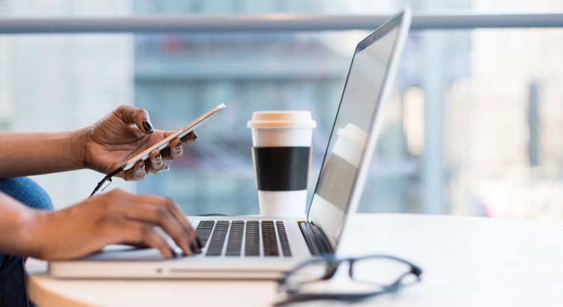 Someone using a laptop, on a desk - whilst holding a phone