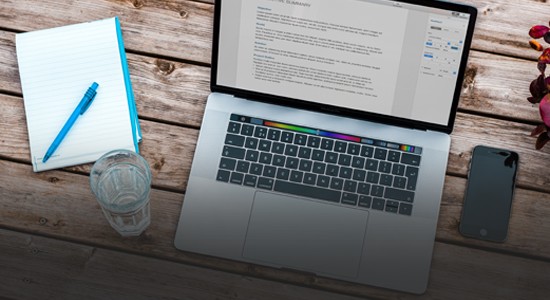 Laptop on a wooden desk, next to a phone and notepad