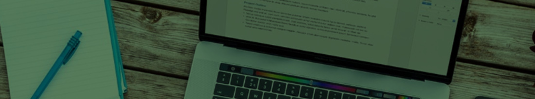 a laptop on a wooden desk, next to a phone and notepad