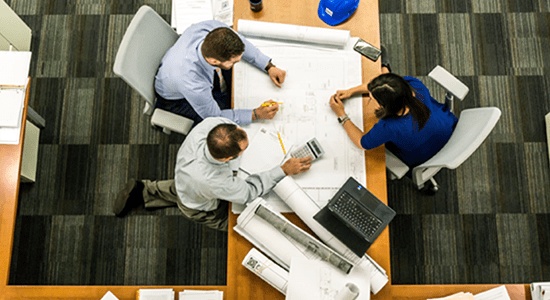 An aerial shot of 3 people sat at a table working collaboratively. 