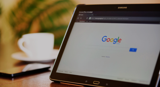 The Google Search interface on a tablet resting on a desk, with a coffee mug and plant in the background.