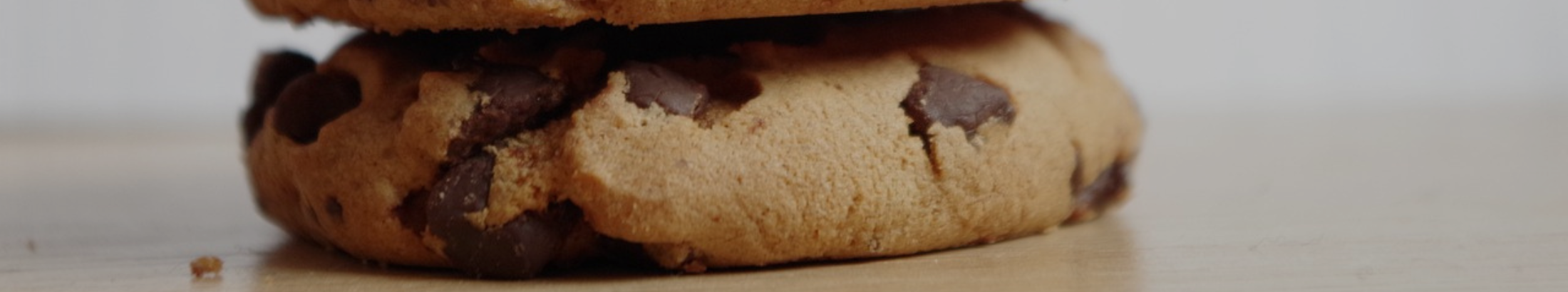 A stack of three chocolate chip cookies on a desk.