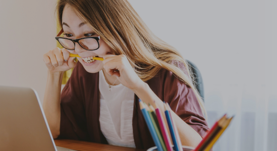 A person biting a pencil in frustration while sitting at her laptop.