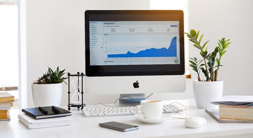 Apple Mac desktop computer on a white desk, surrounded by office accessories